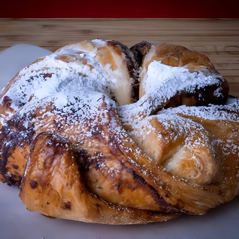 Close-up of a House of Bagels chocolate babka, dusted with powdered sugar, on a white plate.