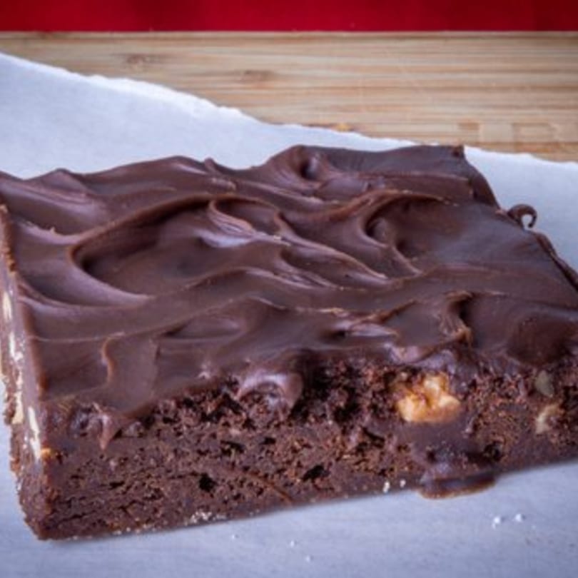 A rich chocolate brownie with thick, swirled chocolate frosting and visible nuts.